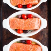 three individual casseroles with tomatoes and fresh salmon fillets ready to be baked