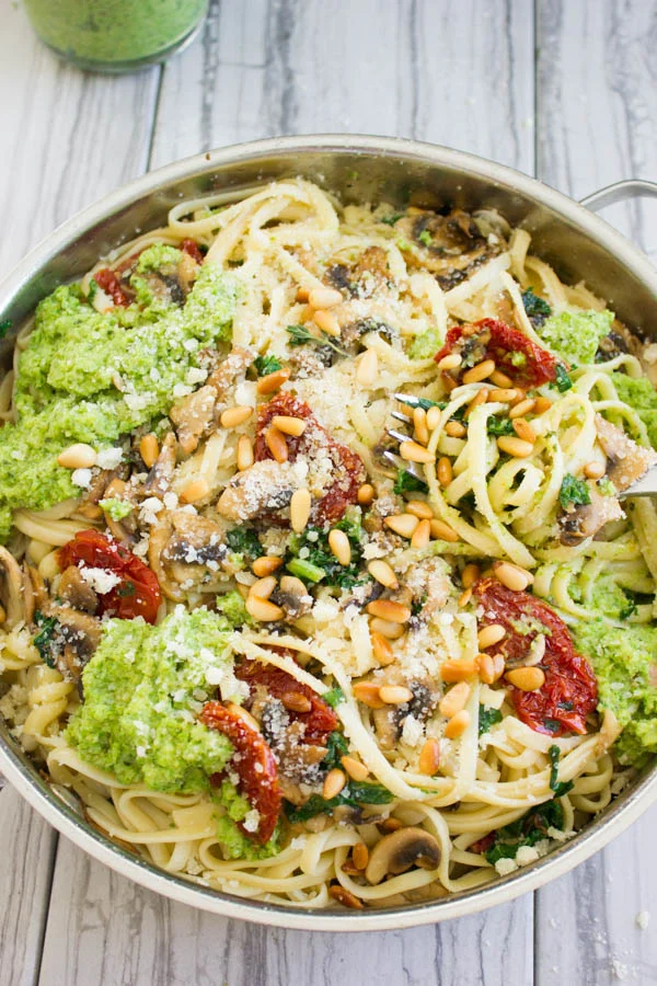 overhead shot of a skillet with pasta topped with broccoli pesto, pine nuts and sun-dried tomatoes
