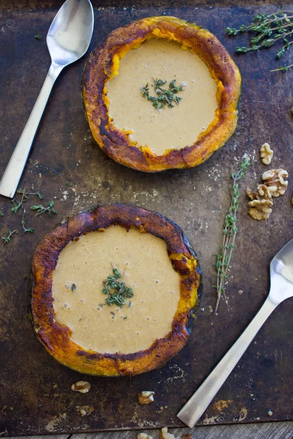 two halved kabocha squashes filled with vegan squash soup with walnuts