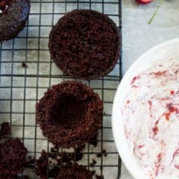 a hollowed out chocolate muffin next to a bowl of cherry whipped cream