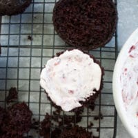 a chocolate muffin being filled with whipped cream and cherries to make black forest cupcakes