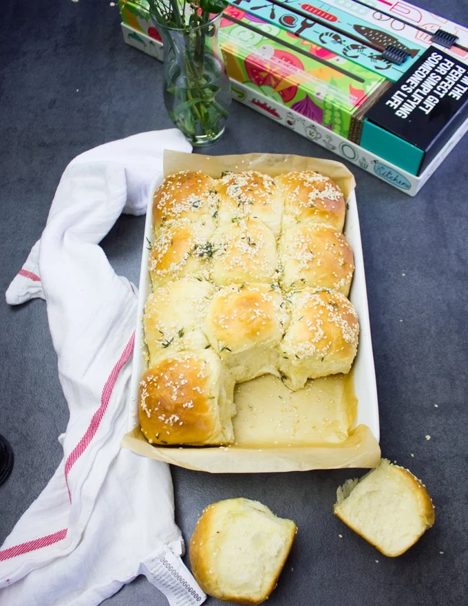 A tray of homemade dinner rolls with two rolls out of the tray on the board showing the insudes of the dough