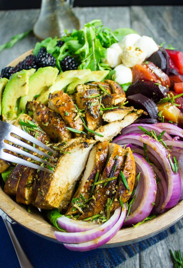 a fork piercing into a juicy slice of balsamic chicken breast on a salad
