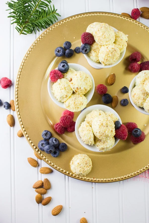 overhead shot of Almond Crunch Greek Yogurt Cheesecake Bites arranged on a golden plate with some fresh berries
