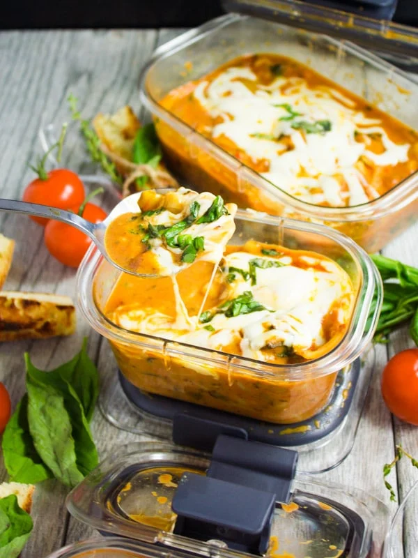 a spoon of lasagna soup with cheese running down the sides over a rubbermaid container with soup