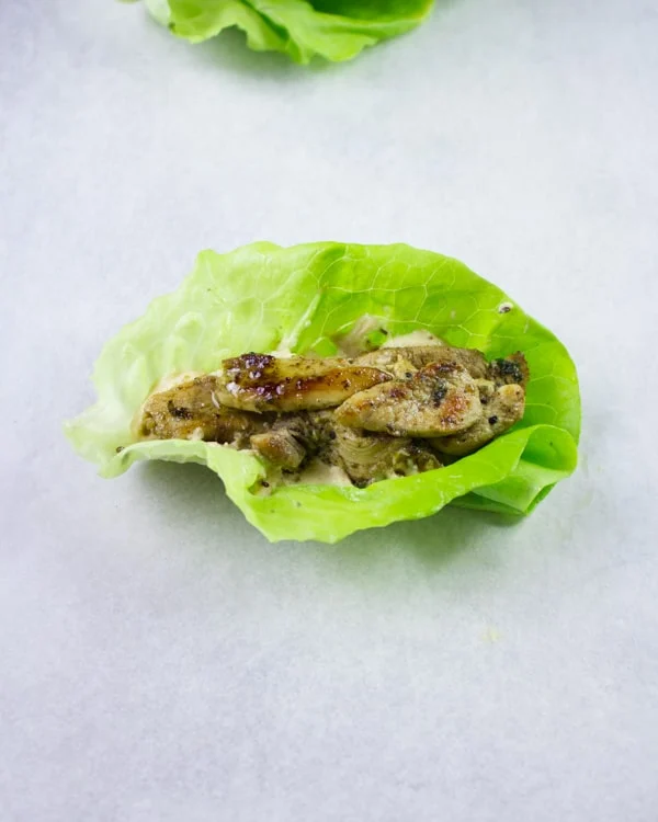 Chicken Shawarma placed on top of a dollop of hummus on a lettuce leave