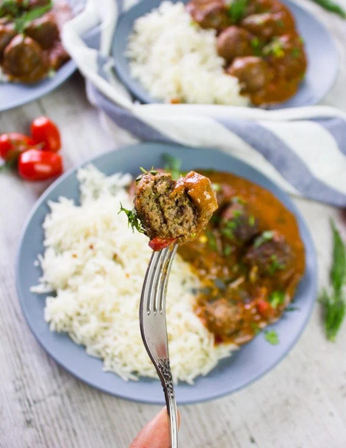 A fork holding a meatball over the plate