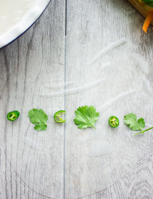 cilantro leaves and green chili sliced being arranged on a sheet of rice paper