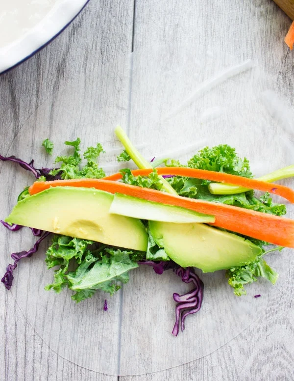 kale, carrot sticks and avocado slices being arranged on rice paper to make rolls