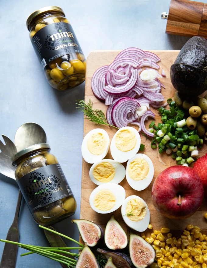 bottled green olives from Morocco on a board next to the hard boiled eggs, sliced onions, jalapenos, ready to go in to the salad
