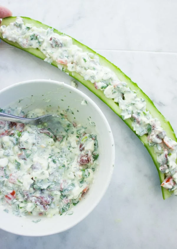 Overhead shot of a cucumber cut lengthwise and filled with feta cream filling next to a bowl with feta filling