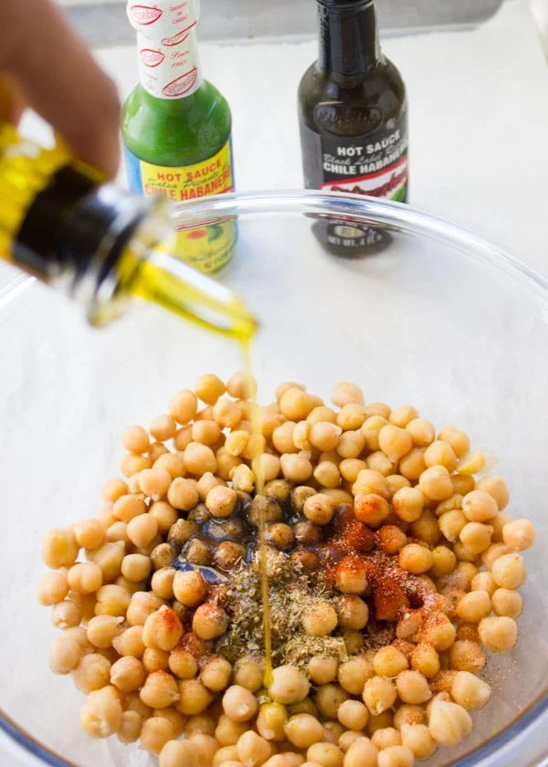 olive oil being drizzled on top of canned chickpeas in a glass bowl