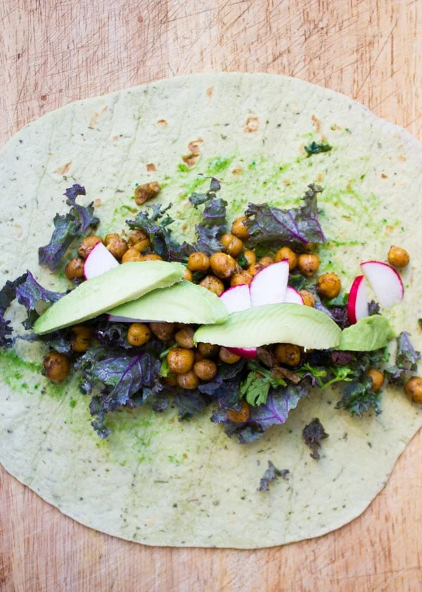 wheat tortilla being filled with roasted chickpeas avocado and veggies to make wraps