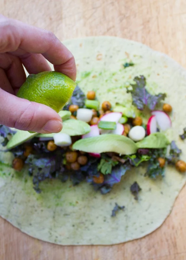 lime being drizzled on top of roasted chickpeas filling piled up on a wheat tortilla
