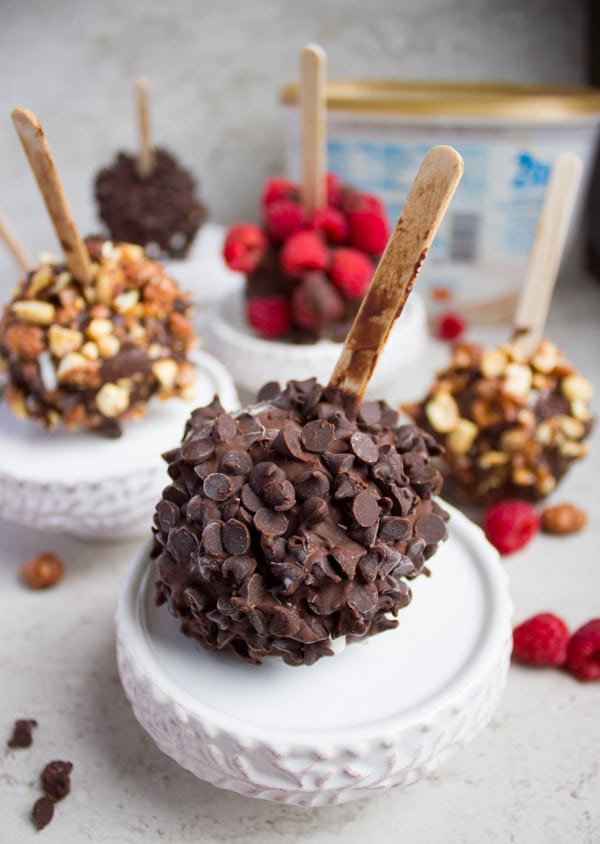 A variety of Ice Cream Pops with different topping on each like chocolate chips, nuts and raspberries.