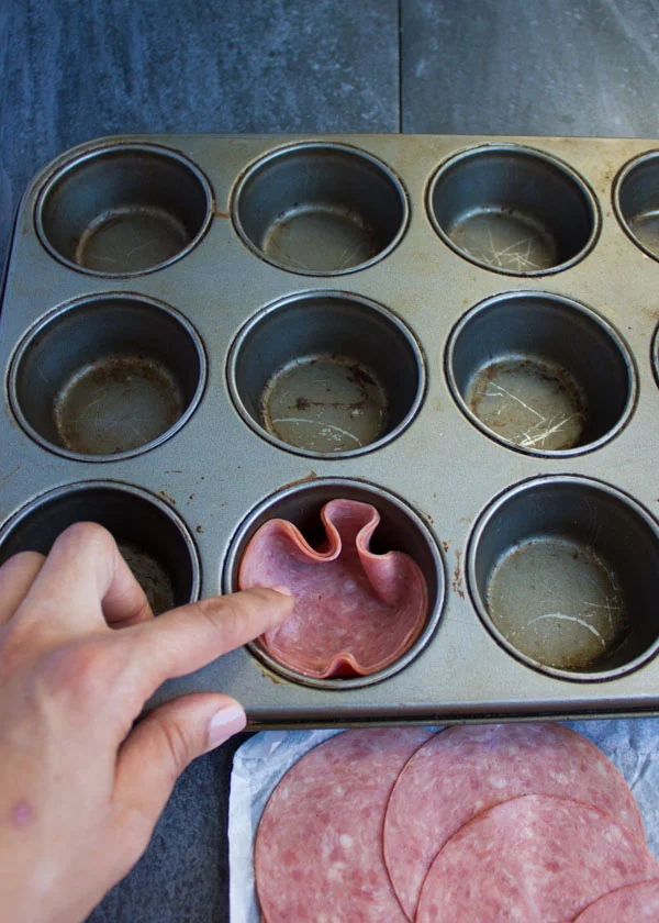 a muffin pan being lined with salami slices to make salami cups