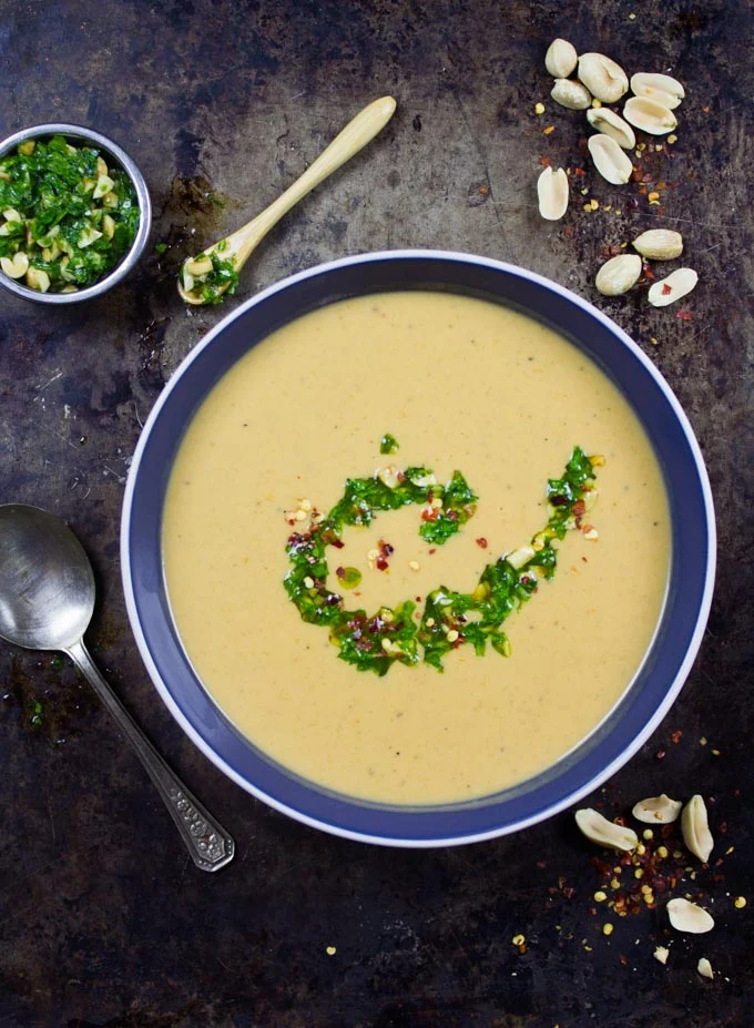 overhead shot of Peanut Soup in a blue bowl with a small spoon and crunchy peanuts