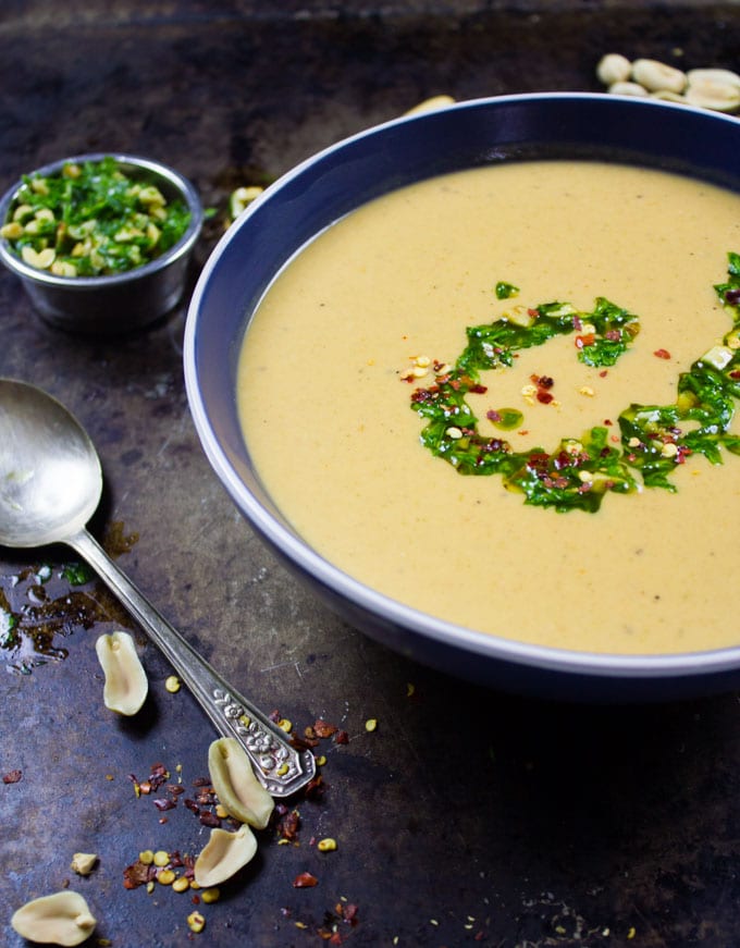 Half a bowl of african peanut soup in a bowl with some crunchy peanuts around it