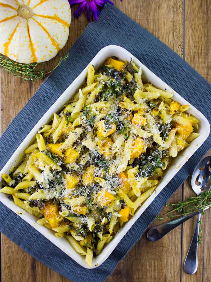 Easy Baked Pasta with Roasted Pumpkin, Kale and Mushrooms in a casserole on a blue place mat with a pumpkin in the background