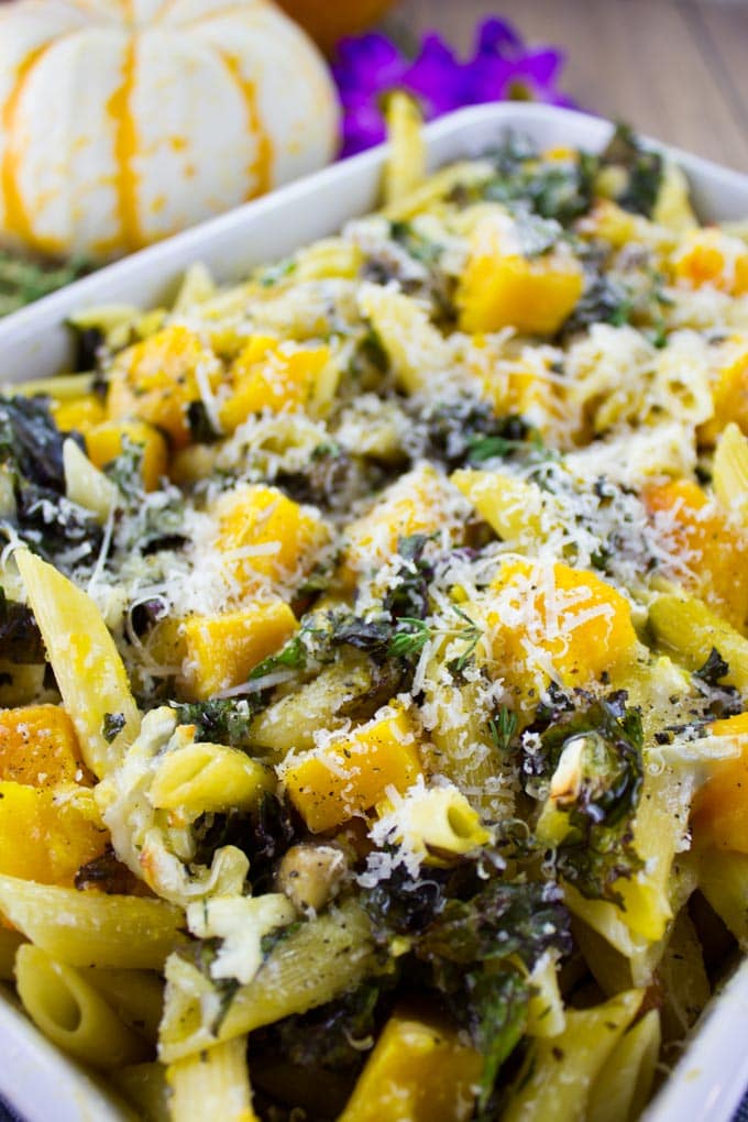 close-up of Easy Baked Pasta with Roasted Pumpkin, Kale and Mushrooms in a casserole with a pumpkin in the background