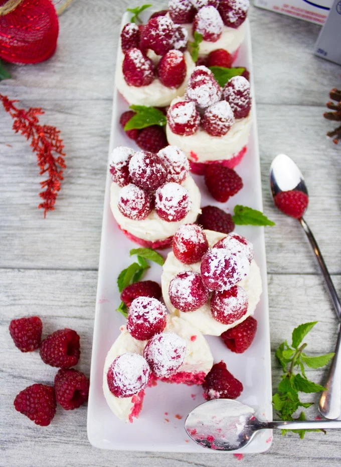 Mini Red Velvet Cheesecake With Sugar Raspberries lined up on a rectangular pate with Christmas decoration on the side