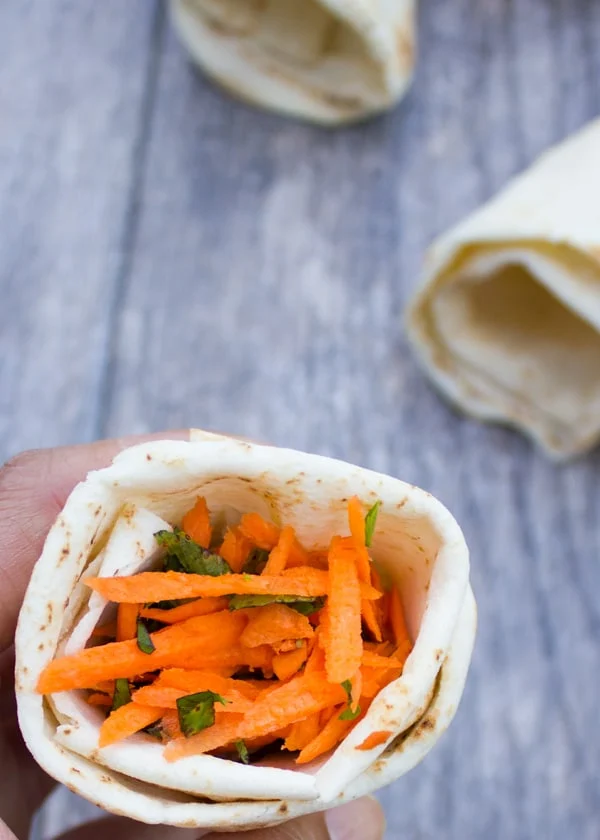 hand holding a pita cone filled with shredded carrots and lettuce.