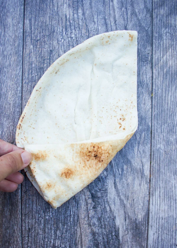 pita bread folded in half placed on a rustic table to demonstrate shaping of pita cones.