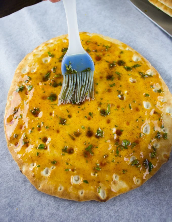 Pita bread being brushed with a mix of herbs and oil to make pita chips