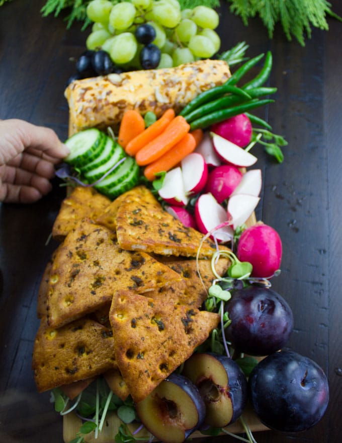 homemade pita chips arranged with sliced veggies and a cheese log