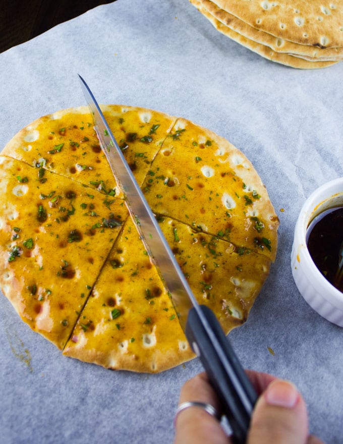 oil and spice covered pita bread being cut into wedges to make pita chips