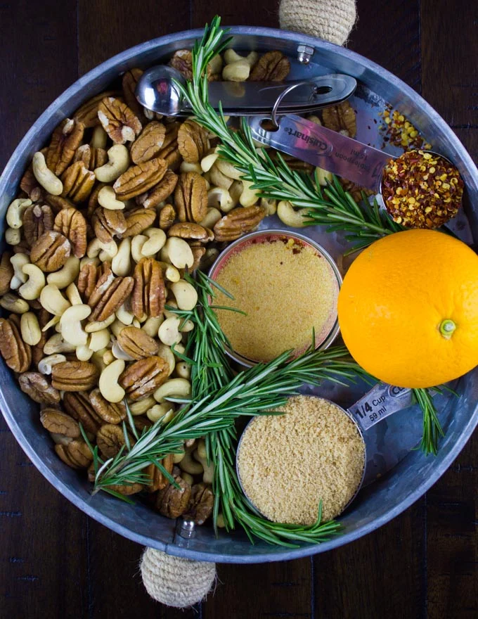 Rosemary Spiced Candied Pecans and cashews in a bowl with some spices and an orange on the side