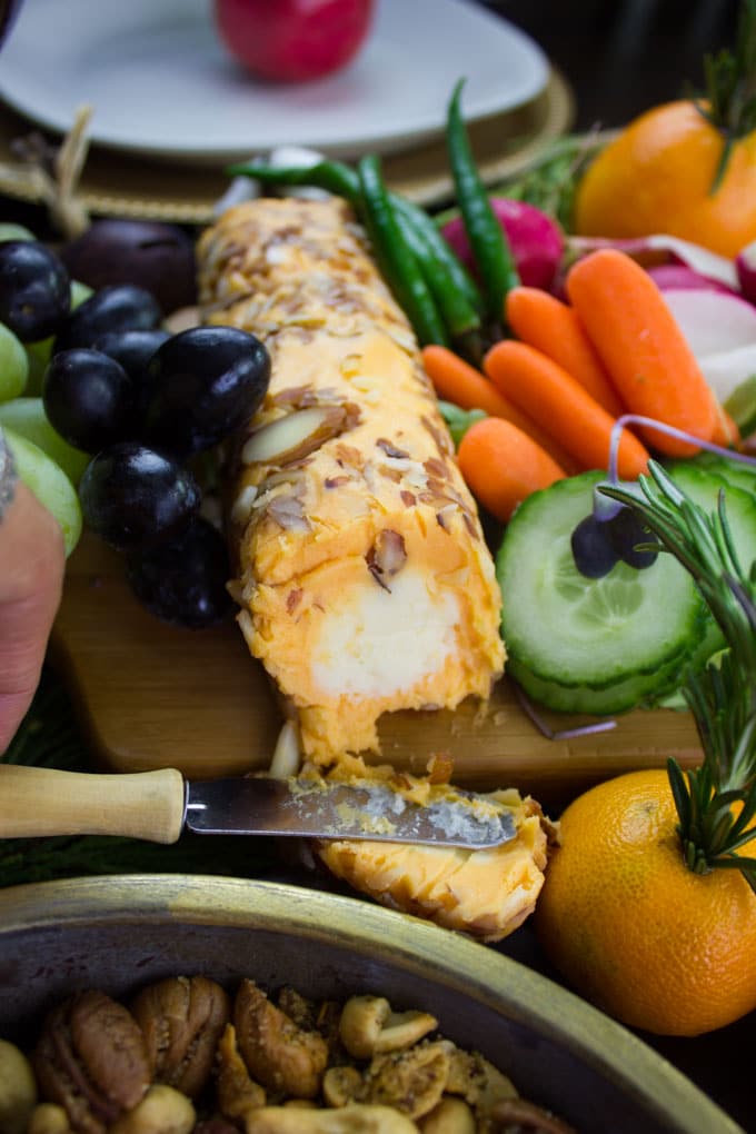 a nut-crusted cheddar cheese log being cut with a knife