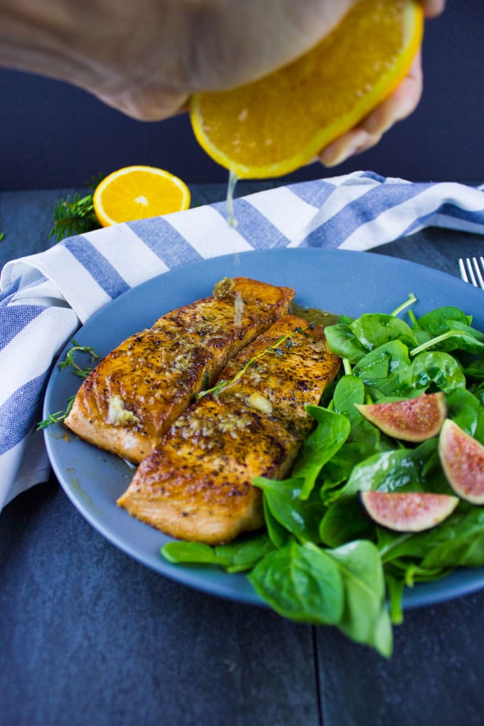fresh orange juice being drizzled on top of two pan-seared salmon fillets
