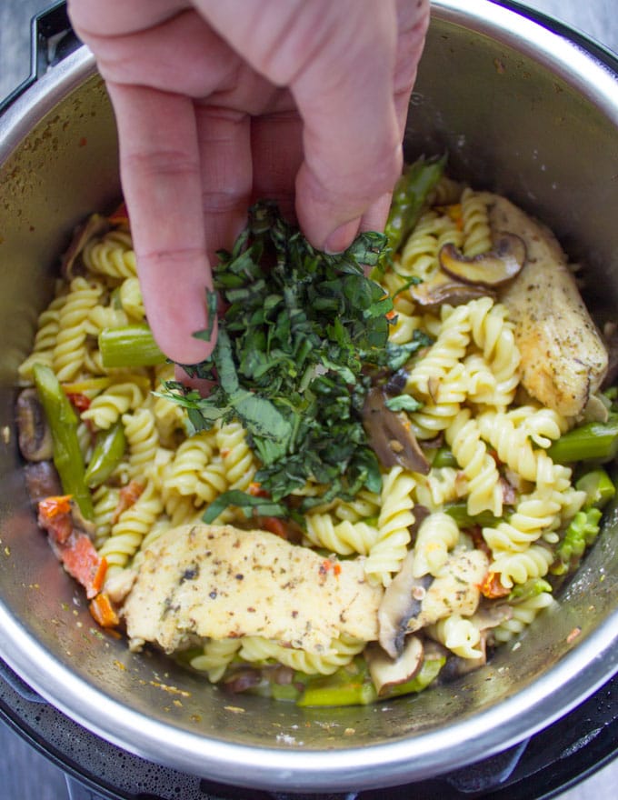 fresh herbs being added to instant pot with chicken pasta