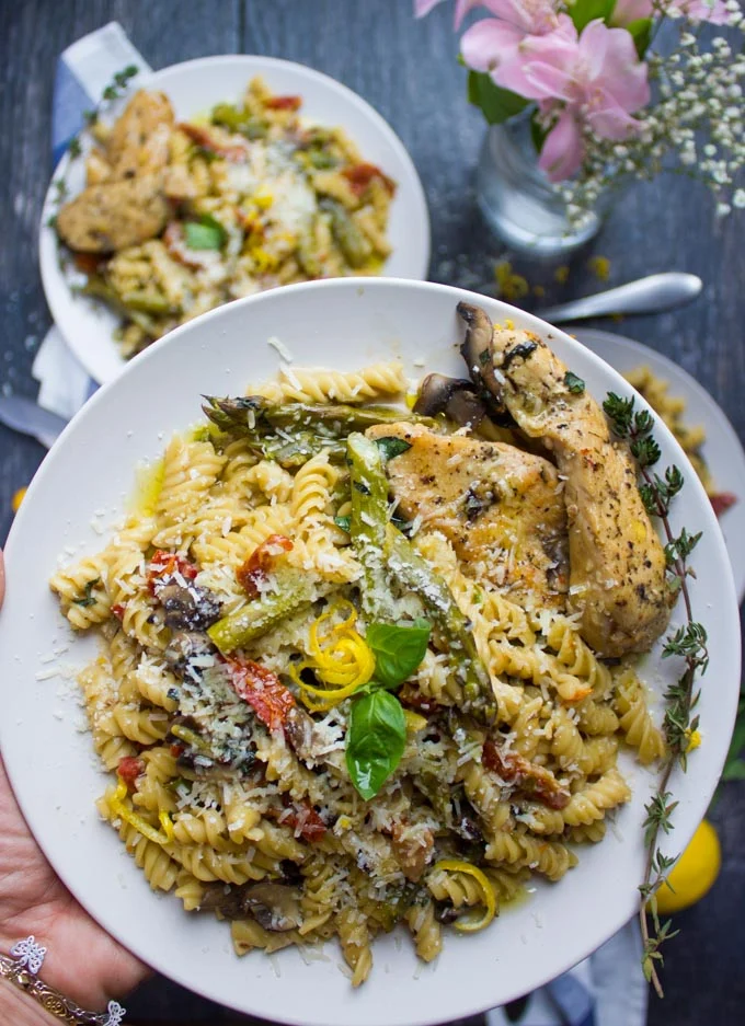 a hand holding a plate of Quick One-Pot Creamy Chicken Pasta
