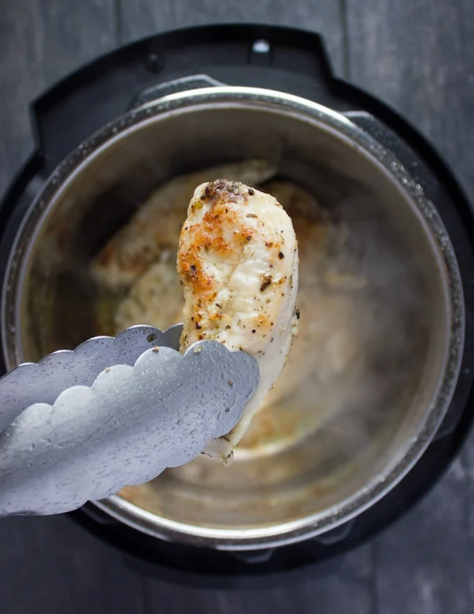 a browned chicken breast being removed from an instant pot with tongues