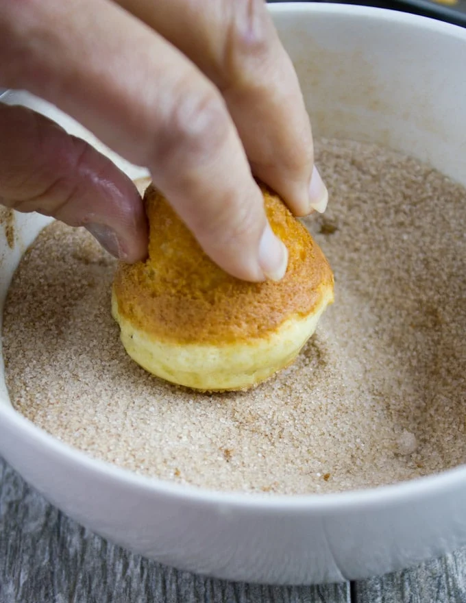 a baked donut hole being rolled in a bowl with cinnamon sugar