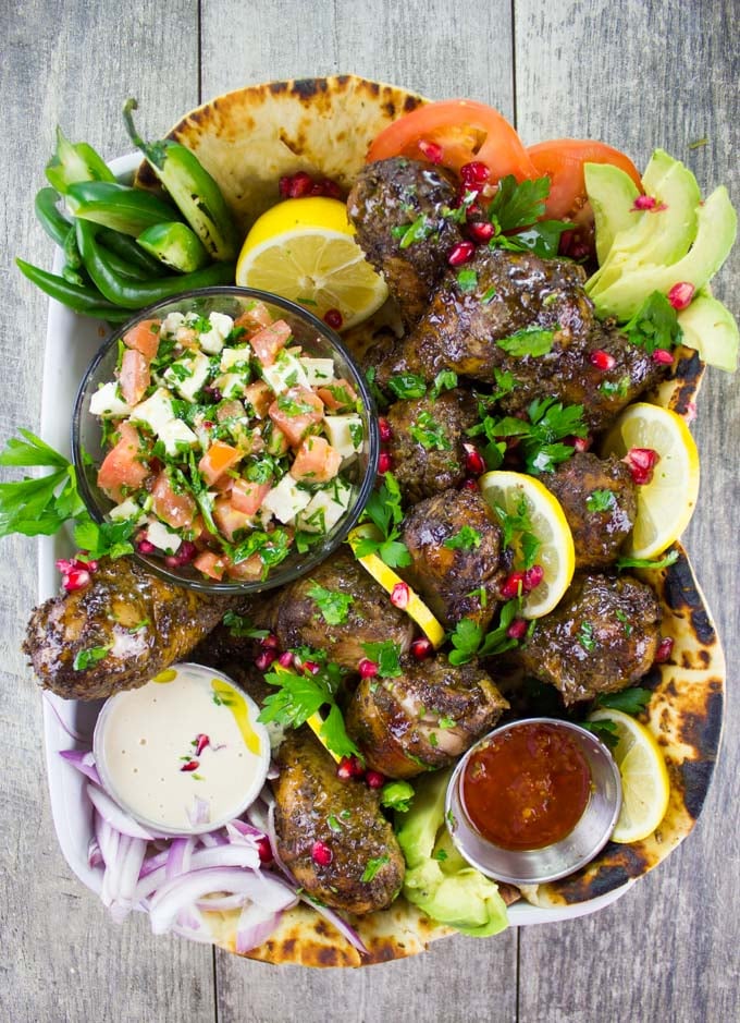 Chicken Shawarma Platter served on charred naan bread with Tahini Sauce, Harissa Sauce and Tomato Feta salad in small dishes nestled in the chicken
