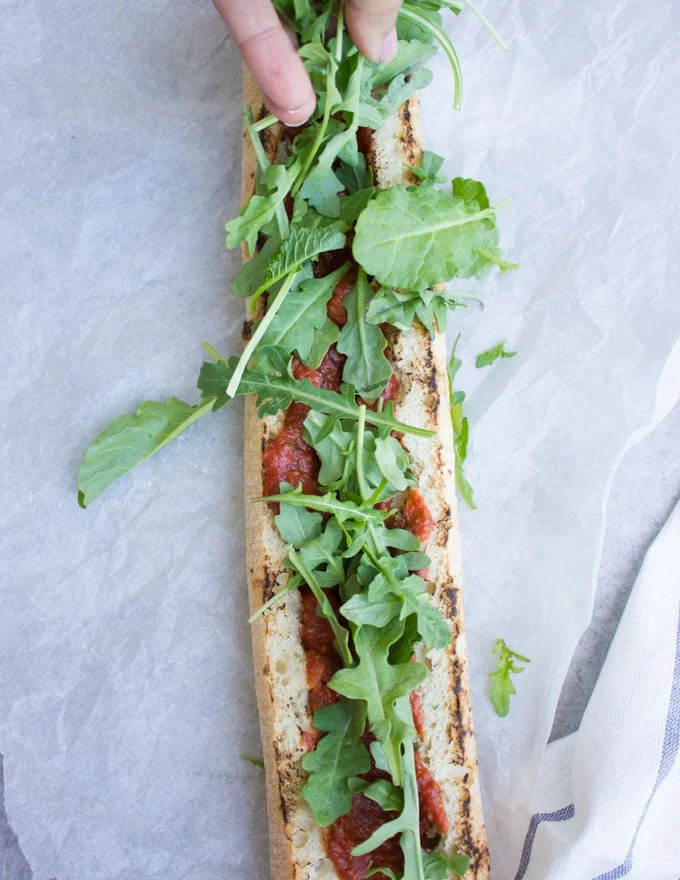 open-faced marinara meatball sub being topped with arugula