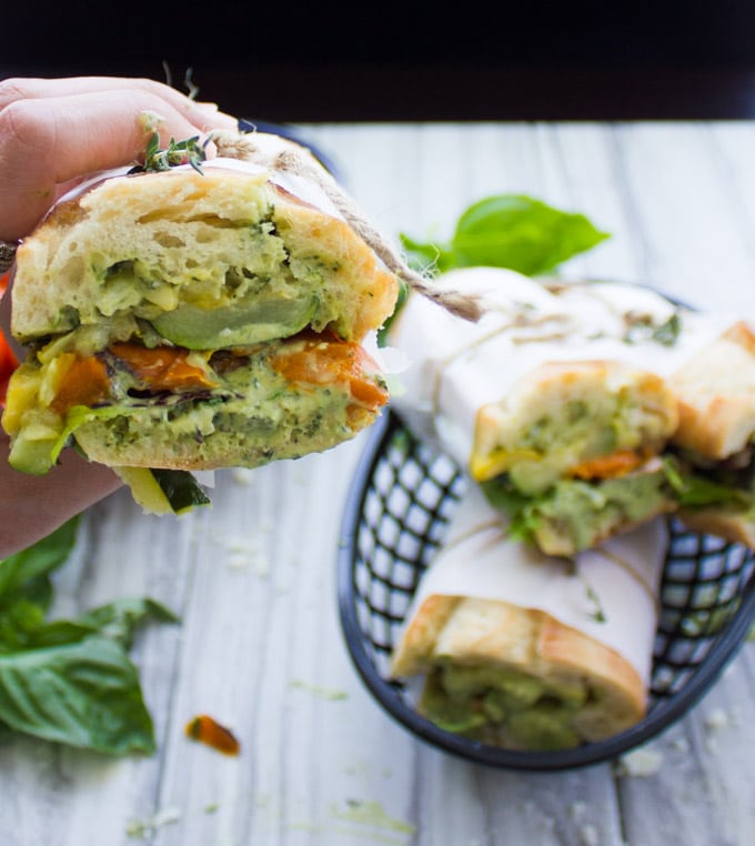 a hand holding half a Roasted Veggie Sandwich with Basil Sauce held together with parchment paper and string