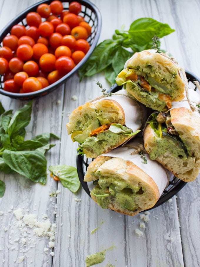four Roast Veggie Sandwiches with Basil Sauce in a black basket with fresh basil on the side