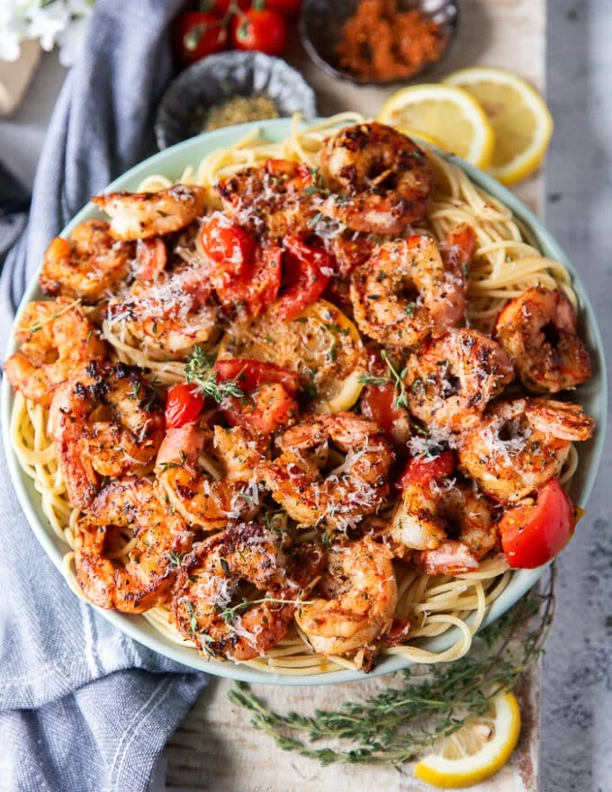 close up of a plate of shrimp pasta with the shrimp on top with herbs, baby tomatoes some feta cheese and lemon slices