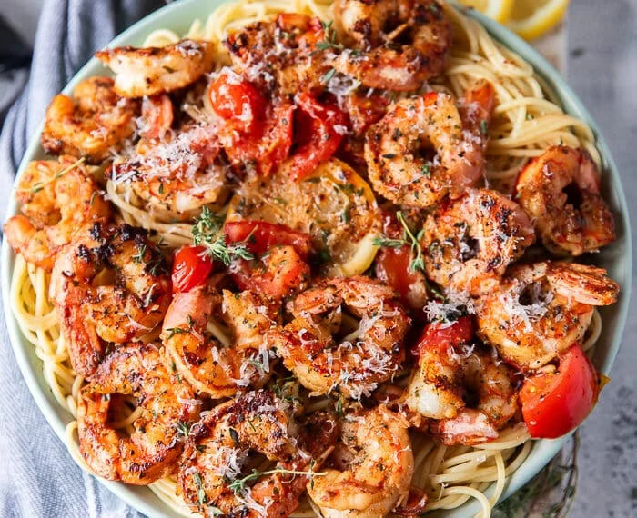close up of a plate of shrimp pasta with the shrimp on top with herbs, baby tomatoes some feta cheese and lemon slices