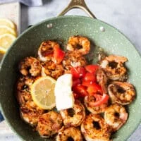 lemon slices, baby tomatoes cut up, butter knobs, herbs and more garlic are added to the cooked shrimp