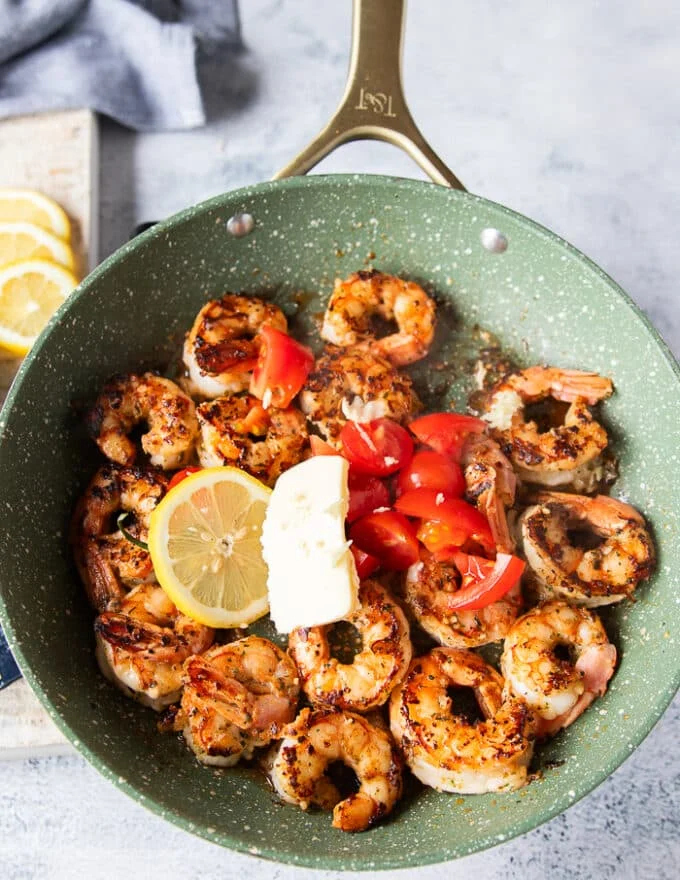 lemon slices, baby tomatoes cut up, butter knobs, herbs and more garlic are added to the cooked shrimp