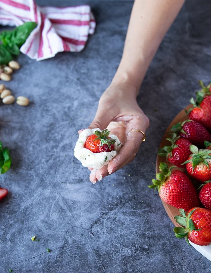 A hand rolling the goat cheese over the strawberries