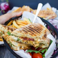 a hand carrying a plate of a split in half sandwich showing the filling of the sandwich