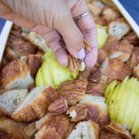 hand sprinkling some pecans over the croissant and pears