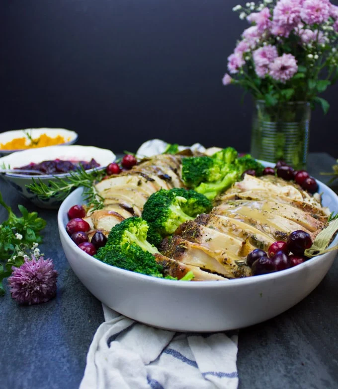 A side view of a platter showing some sliced roasted dry brined turkey breast with gravy drizzled on top.