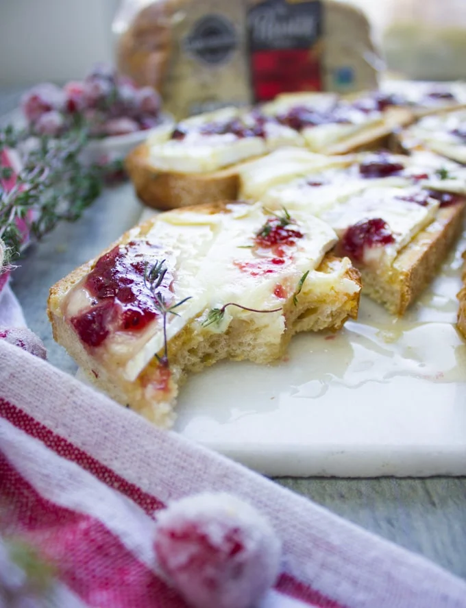 A bitten piece of baked brie toast with cranberry sauce over a white marble